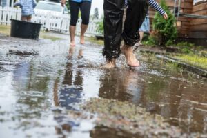 People running barefoot through back yard puddles | Featured Image for the Back Yard Drainage Problems Blog by ASBIR.
